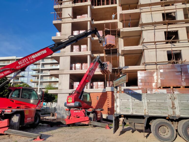 İzmir'de bir inşaat projesinde üst katlara tuğla paleti taşıyan çift Manitou teleskopik vinç çalışması.