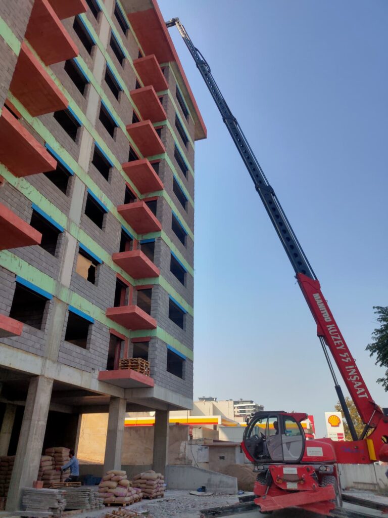 İzmir şehir içinde yüksek katlı binaya dik açıyla tuğla ve malzeme servisi yapan teleskopik vinç.