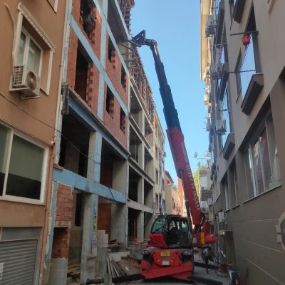 İzmir kentsel dönüşüm projesinde binalar arası dar sokakta çalışan kiralık Manitou vinç ve inşaat süreci.